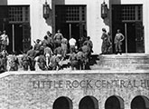 Soldiers stand guard on the steps of Little Rock Central High School as students enter the building, signifying a historic moment during the desegregation efforts in the 1950s.